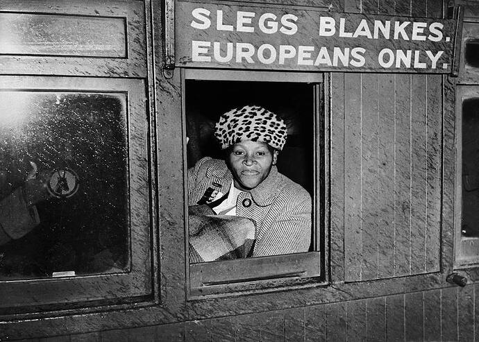 A brave woman sits in a wagon reserved for white people in defiance of apartheid laws, protesting against racial segregation in South Africa. This act of resistance took place in 1952