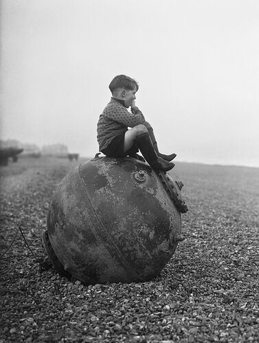 A boy enjoys his ice cream as he sits on a sea mine washed up on the beach at Deal in Kent, February 1940