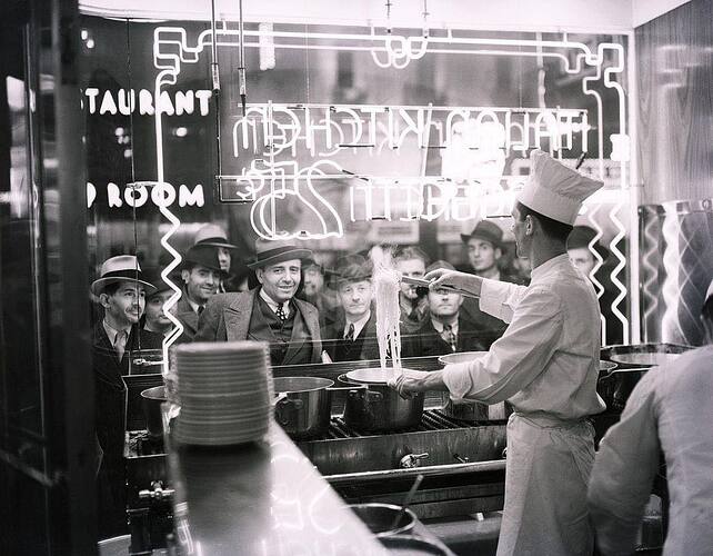 Pedestrians look through a restaurant window to watch a cook prepare a pot of spaghetti in New York City 1937