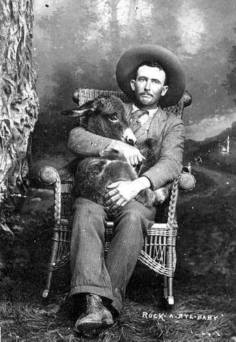 A man posing with a donkey in his lap, 1910s