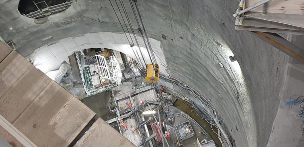 A picture of the back of the Thames Tideway Tunnel Boring Machine Rachel named after Rachel Parsons. The machine is 90 meters or 295 feet long. The image shows the shaft down to the Thames Tideway Tunnel, the tunnel opening, a smaller tunnel connecting to another site above and a crane moving material down to the machine. (MyrtleGal / CC BY-SA 4.0)
